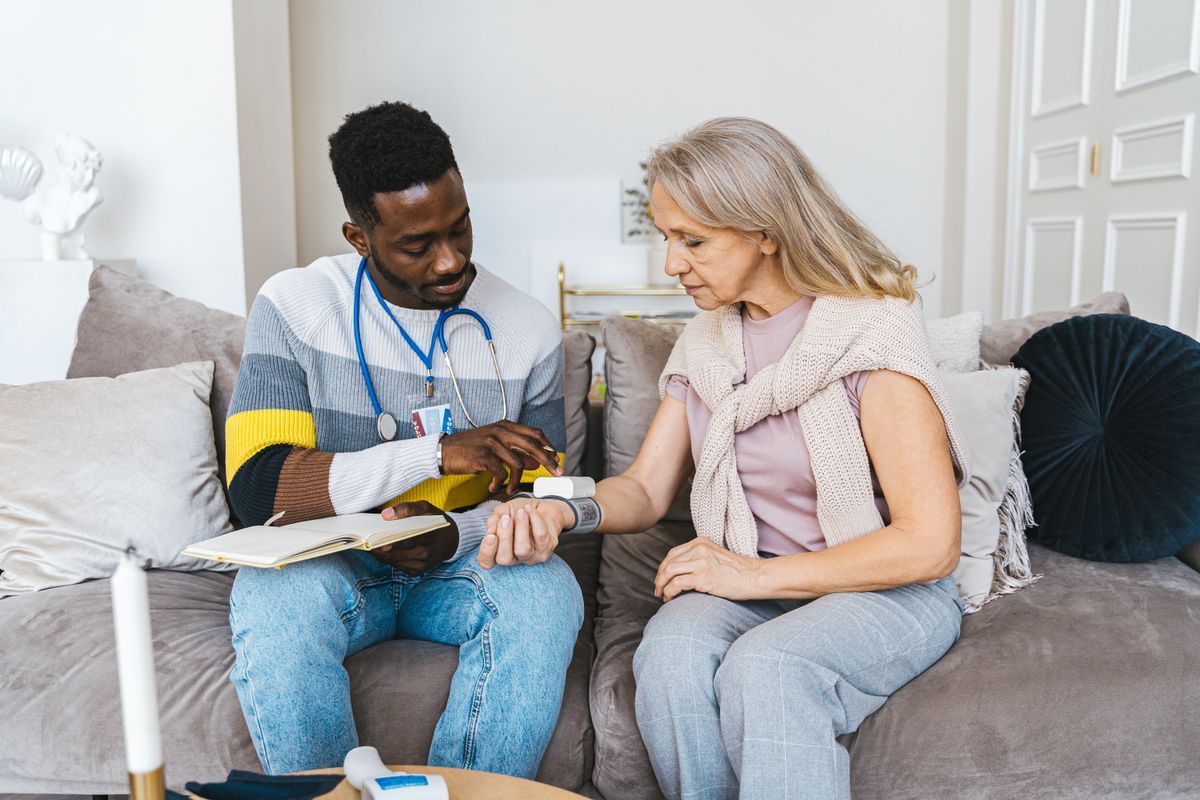 Pflegekraft misst bei einem Hausbesuch den Blutdruck einer Patientin